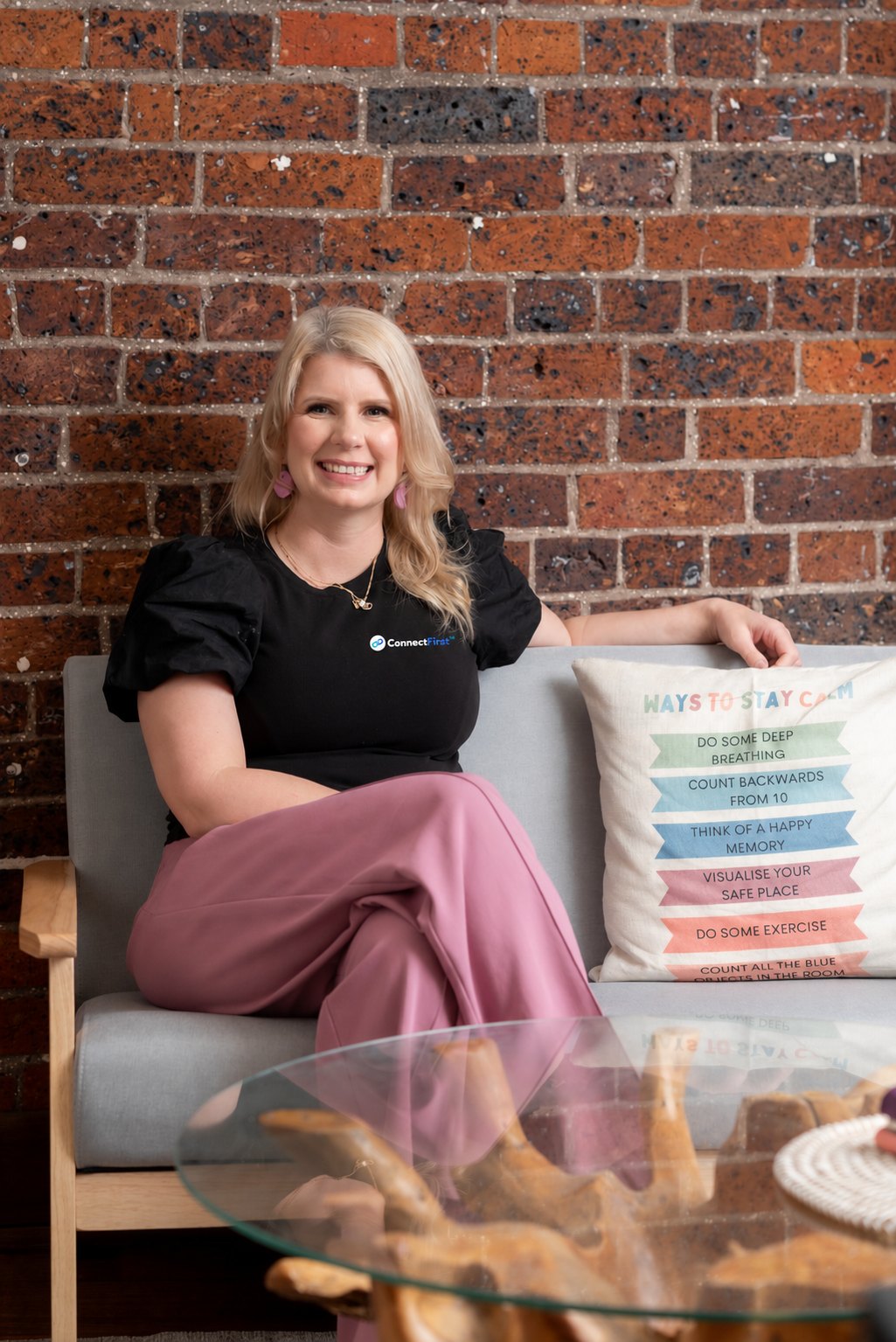 Meg Hughes, founder of ConnectFirst, sitting on a couch in front of a brick wall